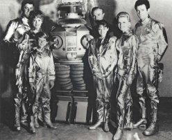 Lost In Space cast wearing silver spacesuits and the robot